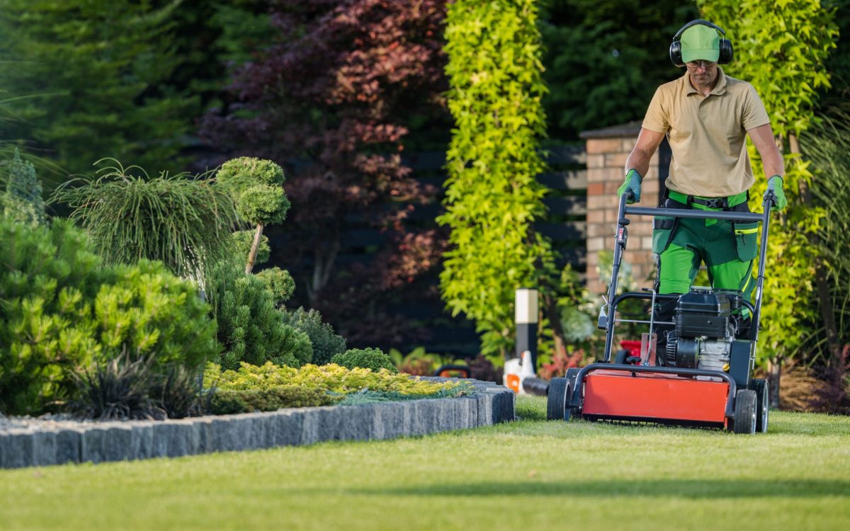 Professional Caucasian Gardener Mowing the Lawn During Backyard Garden Maintenance Work. Gardening Services and Equipment.